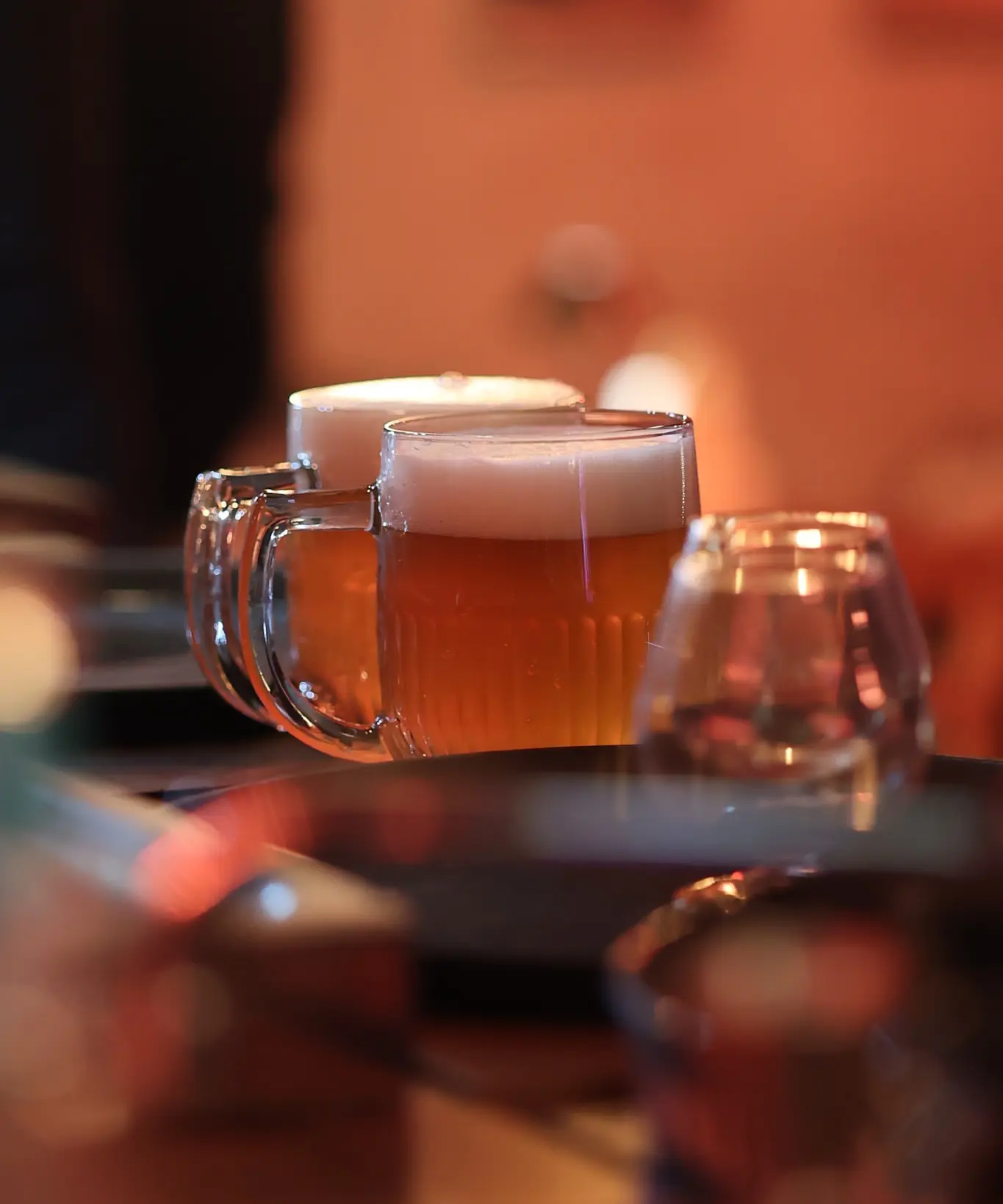 Due boccali di birra ambrata e un calice sul tavolo