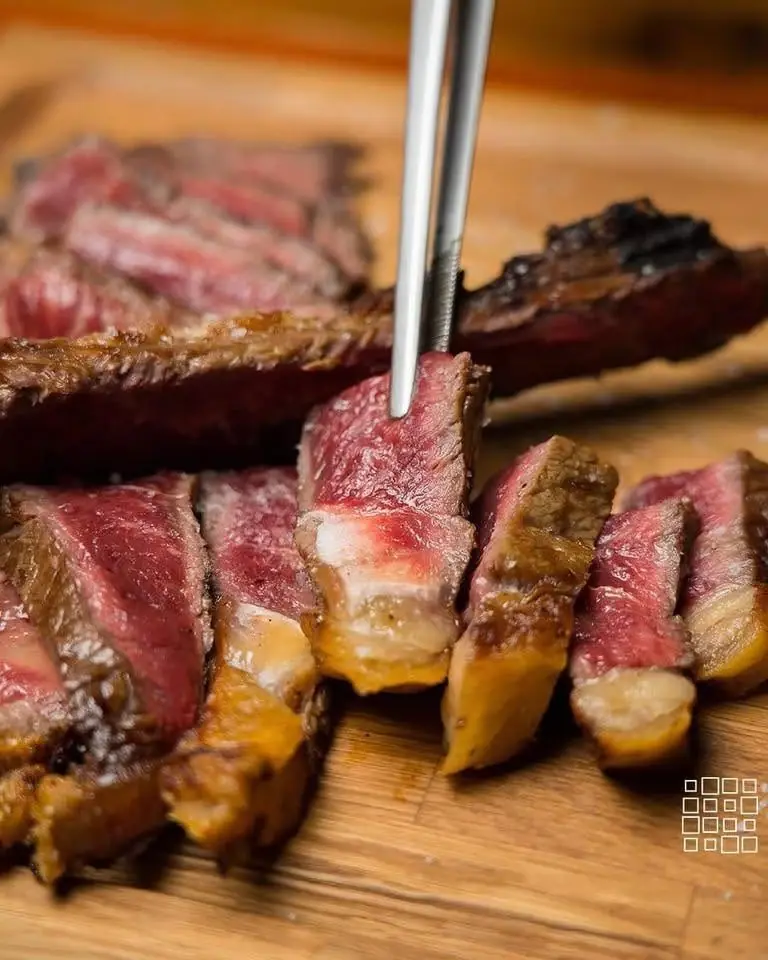 Tagliata di manzo alla brace, rosata al centro, su un tagliere di legno